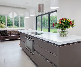Bespoke kitchen island with white quartz worktop, integrated appliances and garden views, designed and built by Nureno in Berkshire