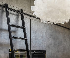 Bespoke kitchen detail with integrated ovens, concrete-effect cabinetry and library ladder, designed and built by Nureno